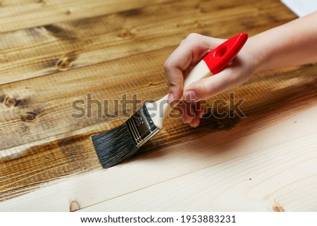 hand holds a paint brush on a wooden background. painting wood with antiseptic impregnation. timber protection concept Royalty-Free Stock Photo #1953883231