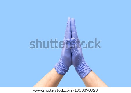 Hands in latex medical gloves folded together indicating the process of prayer. Pray about quick and easy treatment. Good cleaning. Palms isolated on blue background. Close-up. Banner. Medicine hope.