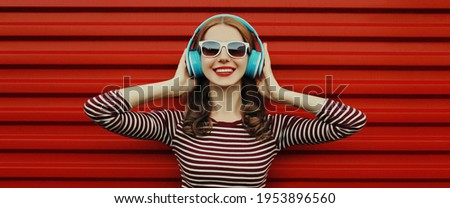 Portrait of cheerful smiling woman in blue headphones listening to music on a red background