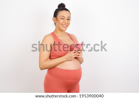 Beautiful pregnant woman in sports clothes against white background taking a selfie  celebrating success