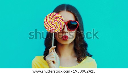 Portrait close up of young woman blowing her red lips with lollipop on a blue background