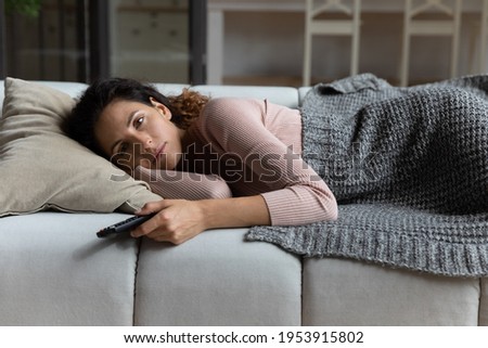 Good night. Sleepy young latin woman lie on sofa late at evening watch tv before fall asleep hold remote control. Tired millennial female relax at home after hard work day switch on favorite series