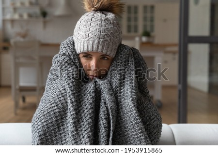 Dull young hispanic woman save herself from freezing wear winter clothes muffle up in blanket think of buying radiator heater. Shivering young lady sit on sofa in plaid ponder on much too cold at home Royalty-Free Stock Photo #1953915865