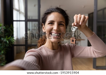 Excited young hispanic lady tenant buyer wish to keep in memory moving to new home take selfie on phone with keys in hand. Happy woman proud of buying flat make video call to friend show key to camera Royalty-Free Stock Photo #1953915904