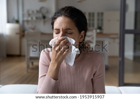 Running nose. Ill latina lady staying at home catching cold rhinitis viral bacterial infection using hygienic one time handkerchief. Young female suffer from seasonal allergy blow nose in paper tissue Royalty-Free Stock Photo #1953915907