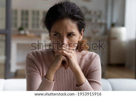 Got to be a way out. Thoughtful unhappy latin female sit on couch with sad look clench fists ponder on life love problem. Anxious doubtful young woman hesitate feel unsure ponder on difficult decision Royalty-Free Stock Photo #1953915916