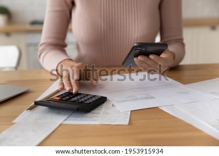 Close up of young female use phone calculator to manage financial documents bills invoices pay utilities calculate business commercial cost income. Hands of woman count loan rent tenancy lease payment Royalty-Free Stock Photo #1953915934