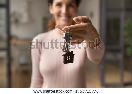 Please take your keys. Close up blurred portrait of smiling young latin lady real estate owner seller propose you client to get key from new home flat. Focus on female broker hand giving bunch of keys Royalty-Free Stock Photo #1953915976