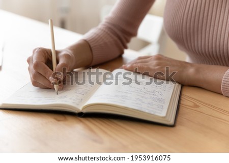Close up view of millennial woman sit at table hold pencil take notes to paper notebook working studying. Female student businesswoman employee write records to daily planner by hand at home work desk Royalty-Free Stock Photo #1953916075