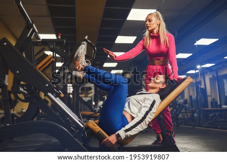 Woman Personal trainer helping other woman in works out on training apparatus inside in fitness center. Sporty lifestyle, bodybuilding, training concept. High quality photo