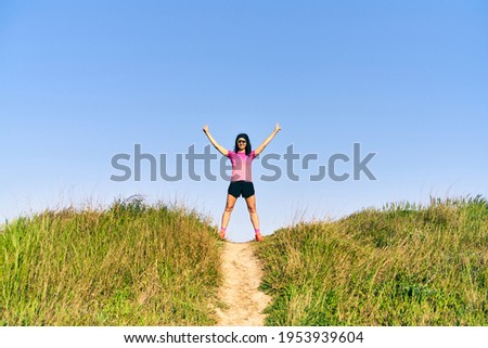 Woman making the victory sign at the top of the track on a straight and stretch path in a grass field.