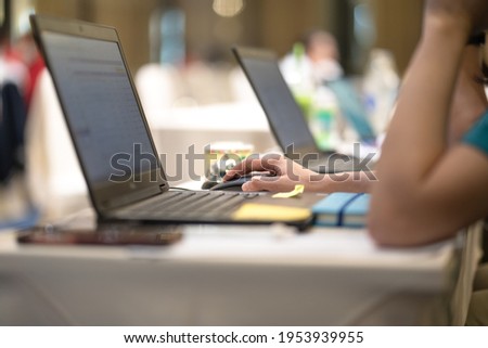 Action of a business person is clicking on mouse to working on the laptop, with blurred background of bokeh lighting of business meeting environment. Close-up and selective at person hand.
