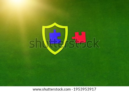 The shield is yellow, the two puzzle pieces are blue and red on a green background. The concept of protection, activity insurance.
