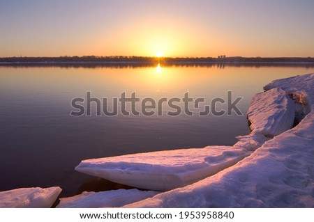 Morning on the bank of the Ob. A broken ice floe on the surface of the river water, the rising sun on the horizon. Novosibirsk, Siberia, Russia
