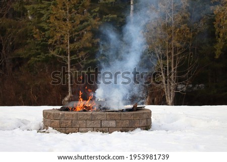 Fire burning in an outdoor firepit in the winter. Smoke rising from a bonfire in a brick fire pit surrounded by snow 