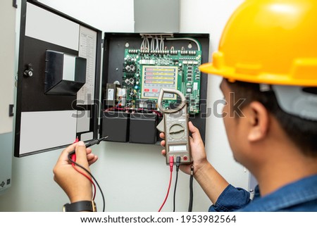Electrician working use digital clamp meter in hands of electrician, close-up against background of electrical wires and relays. Adjustment of scheme of automation and control of electrical equipment Royalty-Free Stock Photo #1953982564