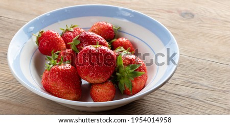 Natural ripe strawberries in a plain white bowl on a wooden table