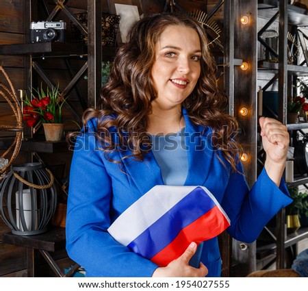 A woman holds the flag of Russia and points to the side. Beautiful female student with Russia flag. Russia study or student exchange program concept. education in Russia. Positive plump woman Royalty-Free Stock Photo #1954027555