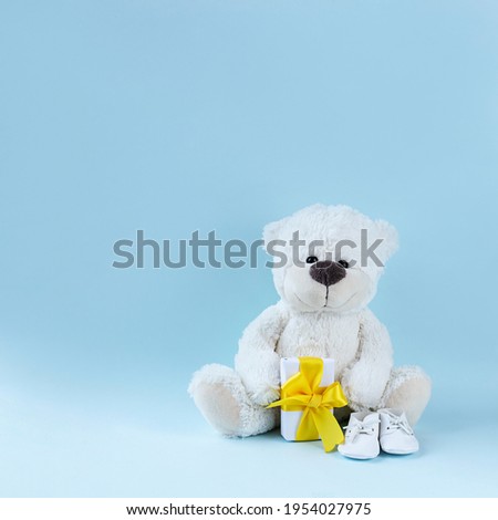 White teddy bear, baby booties and small present with yellow ribbon on light blue background. Greeting card, baby shower invitation, baby birth, gender reveal concept. Square image