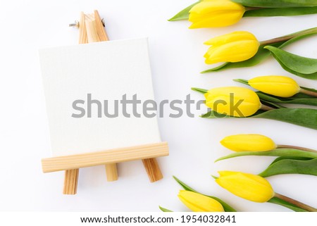 Flat lay with yellow tulip flowers and empty picture frame on white background. Greeting card design for Easter, Mothers day, International womens day or Saint Valentines day