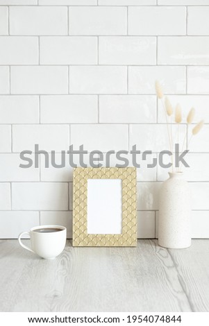 Breakfast still life. Cup of coffee, picture frame mockup and vase of dried flowers on wooden table. Brick tiles wall on background. Hygge, nordic, Scandinavian style.