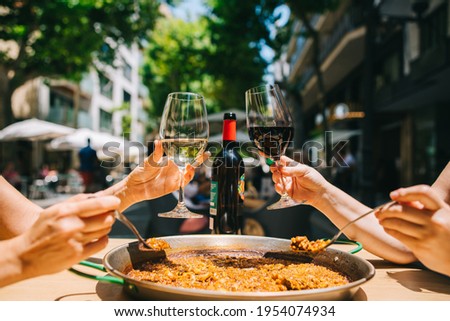 two girls holding drinks wine start eating paella with seafood and squid at a table in a restaurant Royalty-Free Stock Photo #1954074934