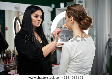 Bride getting ready for wedding. Professional make-up artist applying blush on female clients' face with big makeup brush. Work process in beauty studio. Close-up picture on make-up model.