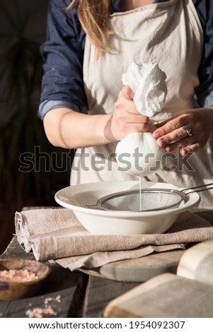 Preparation of cottage cheese - woman straining the milk through a cheesecloth Royalty-Free Stock Photo #1954092307