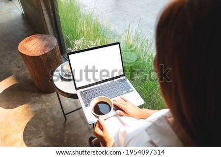 Mockup image of a woman using and touching on laptop touchpad with blank white desktop screen while drinking coffee in cafe