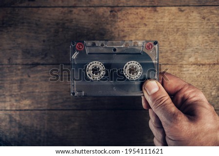 Hand holding audio cassette tape on brown old wooden table. Minimalism retro style concept. Background pattern for design. 