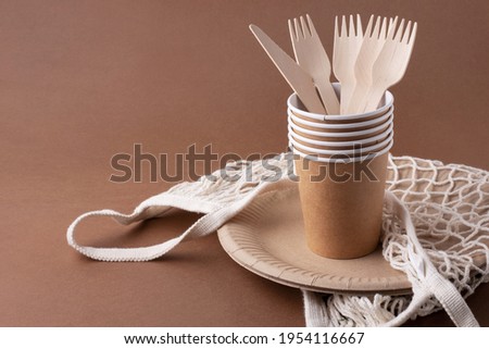 paper bag with handles, disposable eco friendly tableware, plates, glasses, Cutlery, on a brown background, front view of eco waste