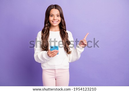 Photo of young beautiful smiling pretty girl pointing finger copyspace hold smartphone isolated on violet color background