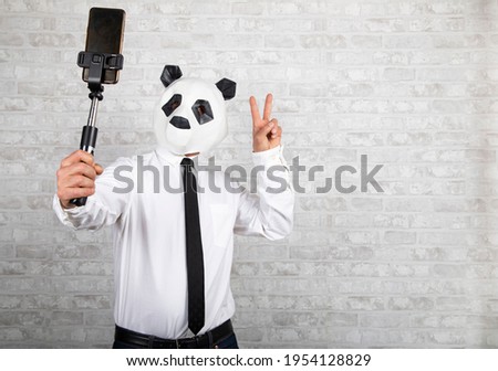 A businessman wearing a panda mask with a sympathetic gesture takes a photo with his mobile phone
