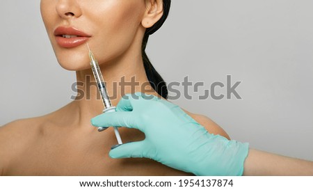 Lips filler injection for beautiful woman's lip augmentation with beautician on grey background. Lip augmentation procedure