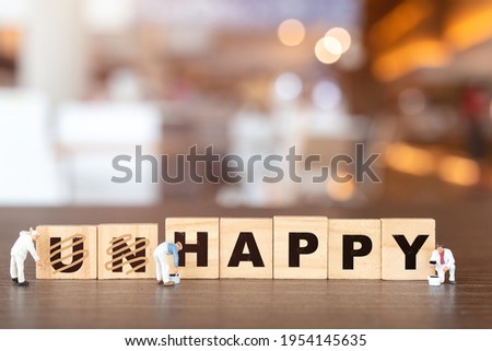 Miniature  people worker team on Unhappy word in wooden alphabet letters with prefix un crossed out, leaving the word Happy Royalty-Free Stock Photo #1954145635