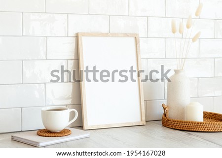 Vertical white photo frame mockup, cup of coffee, vase of dried flowers, candle on wooden table. Nordic, Scandinavian interior room design. Breakfast still life.