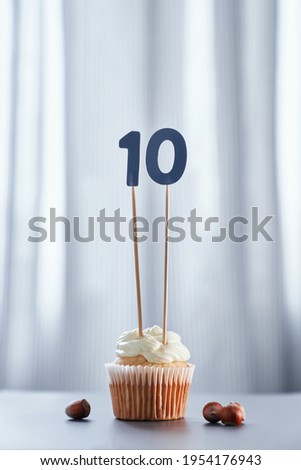 Homemade vanilla anniversary cupcake with creamy topping and number 10 ten with bright background. Minimalistic birthday or anniversary concept. High quality vertical image