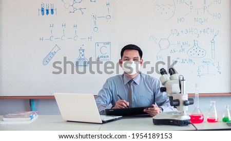 Science chemistry teacher teaching with microscope and laptop in the classroom