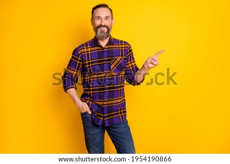 Photo of mature happy man point finger empty space hold hand pocket recommend isolated on yellow color background