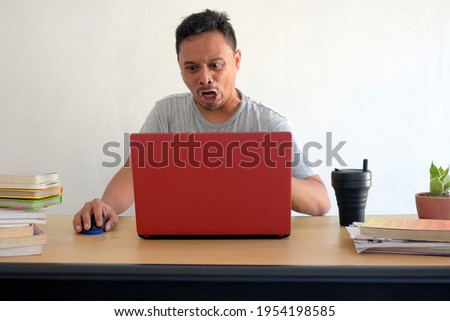 angry reaction of man looking at laptop while work at home, funny rage asian guy in front of computer desk, unfriendly expression face isolated in white