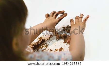 Little girl's hands are covered in chocolate. Dirty children's hands. A child smeared a chocolate cake on the white table at home in the kitchen. The concept of a happy family. Happy childhood.
