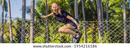 BANNER, LONG FORMAT Young woman on a soft board for a trampoline jumping on an outdoor trampoline, against the backdrop of palm trees. The trampoline board is like a wakeboard, skateboard or snowboard