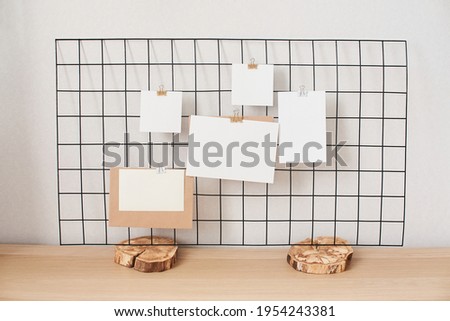 Cards and posters mock ups on black grid board on wooden stand. Blank paper in different sizes attached with binder. Template for prints, photography, to do or planning lists.