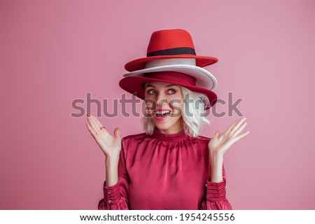 Funny fashionable woman wearing three hats, posing on pink background. Model looking up. Fashion, sale, shopping advertising conception. Copy, empty space for text Royalty-Free Stock Photo #1954245556