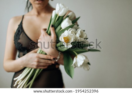 A girl in a black bodysuit without a face holds a bouquet of white tulips in her hands. Horizontal photo