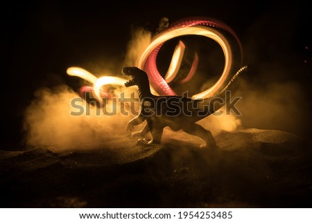 Silhouette of giant Dinosaur in foggy night. Creative decoration with little miniature. Burning misty background. Selective focus