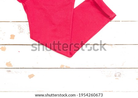 Photography of clothes of a red pants on white wood. The photo has a small space to put text. The photograph is an overhead shot with a horizontal format.