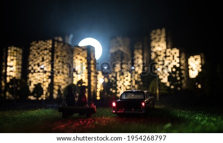 Cartoon style city buildings. Realistic city building miniatures with lights. background. Romantic couple sitting in from of nigth city in selective focus