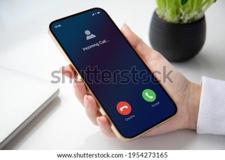 female hand holding golden phone with incoming call on screen in the office  Royalty-Free Stock Photo #1954273165