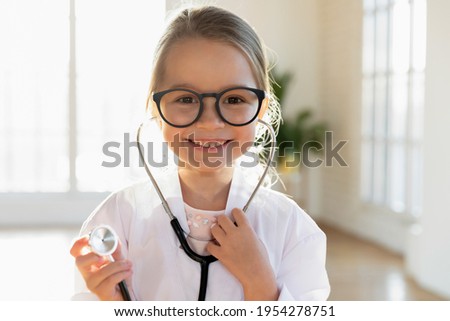Close up headshot portrait of cute little Caucasian girl child in medical uniform stethoscope play act doctor. Profile picture of small smiling kid have fun enjoy hospital game. Healthcare concept.